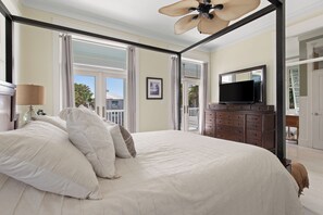 A bedroom with a large bed, a TV on a dresser, and a balcony with curtains.
