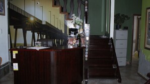 A reception desk with a wooden finish, a staircase with a decorative railing, and a potted plant on a counter. - Pousada praia de costazul (Rio das Ostras)