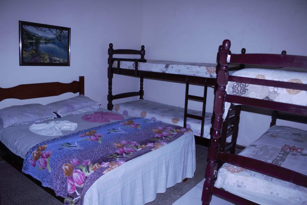 Une chambre avec des lits superposés, un lit recouvert d’une couette à motifs floraux et un tableau encadré accroché au mur.