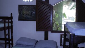 A room with bunk beds, a bed with a striped bedspread, a hanging light fixture, a window with a view of greenery, and a painting on the wall. - Pousada praia de costazul (Rio das Ostras)