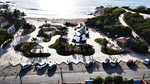 An aerial view of a coastal area with a parking lot, a beach, and a park with walking paths and benches. - Pousada praia de costazul (Rio das Ostras)