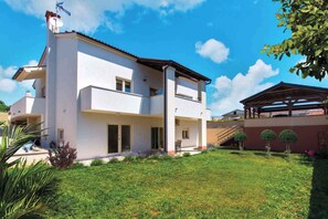 Una casa de dos pisos con techo plano, antena parabólica y un patio cubierto.