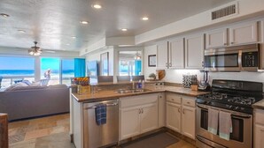 Cucina moderna con mobili bianchi, elettrodomestici in acciaio inossidabile e vista sulla spiaggia.