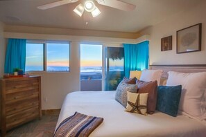 Ein Schlafzimmer mit einem großen Bett, einem Deckenventilator und Meerblick durch große Fenster.
