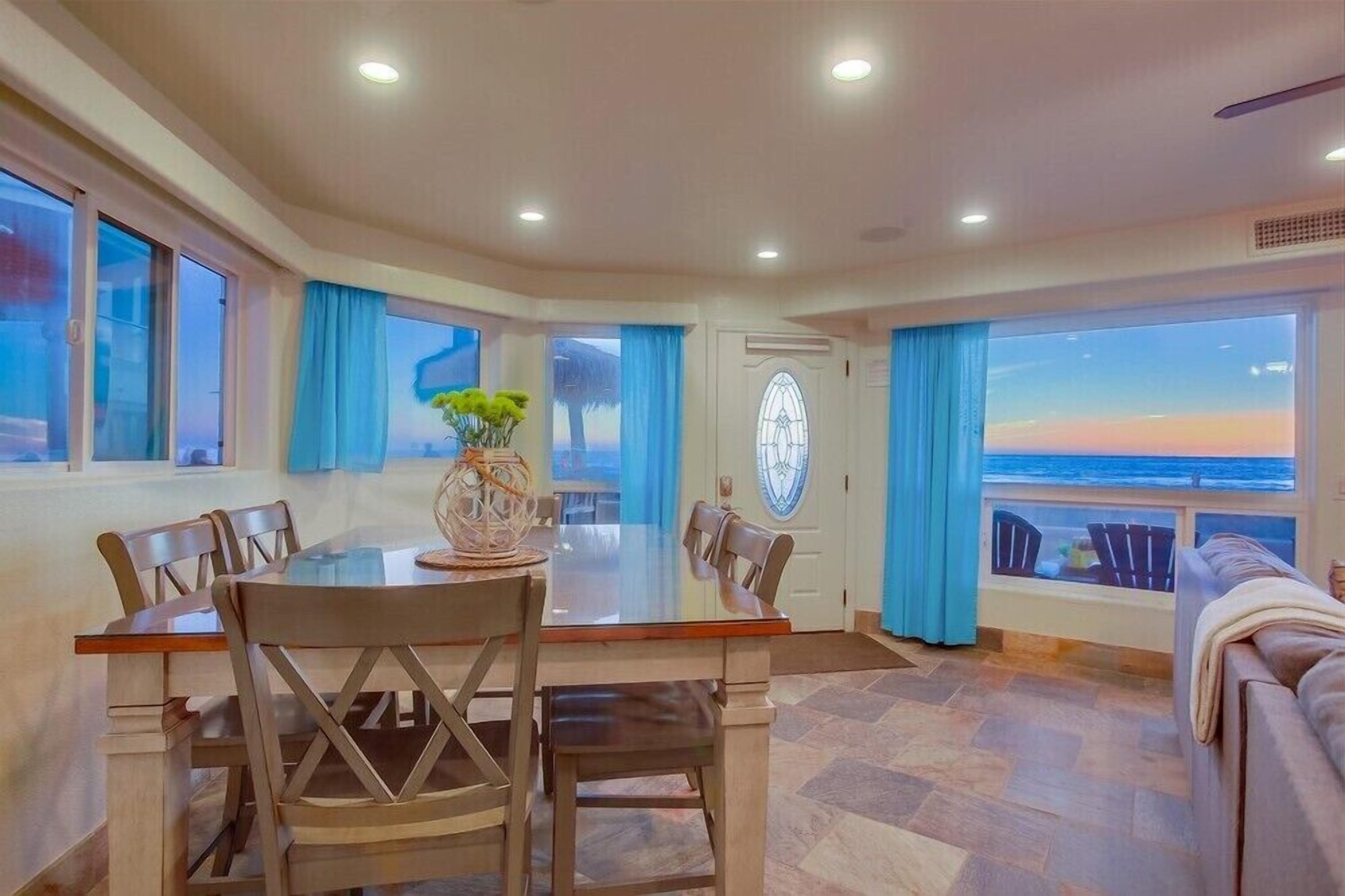 Un coin repas avec une table et des chaises, un vase décoratif et une vue sur l’océan grâce à de grandes fenêtres.