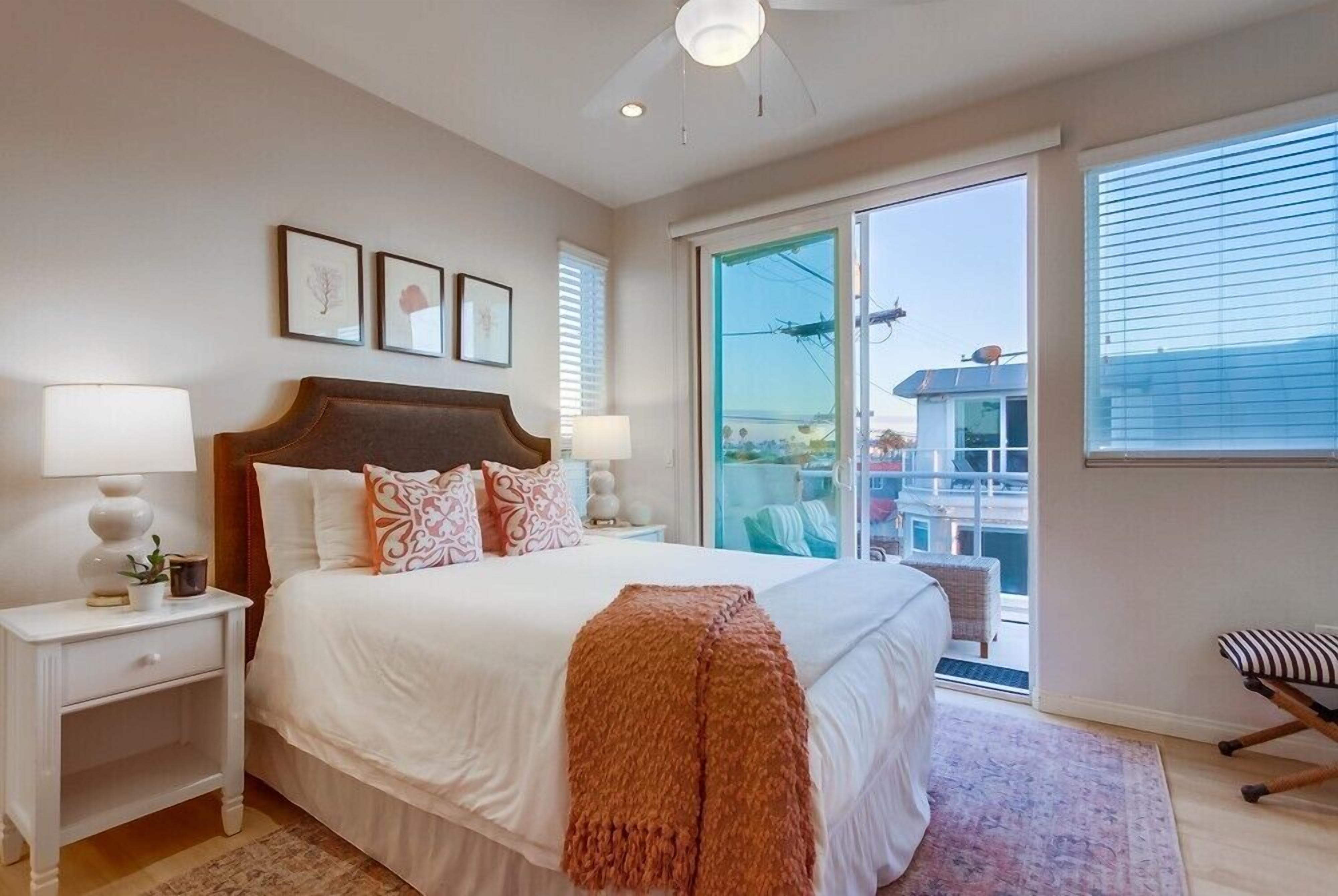 A bedroom with a large bed, a nightstand, a window with a view, and a ceiling fan.