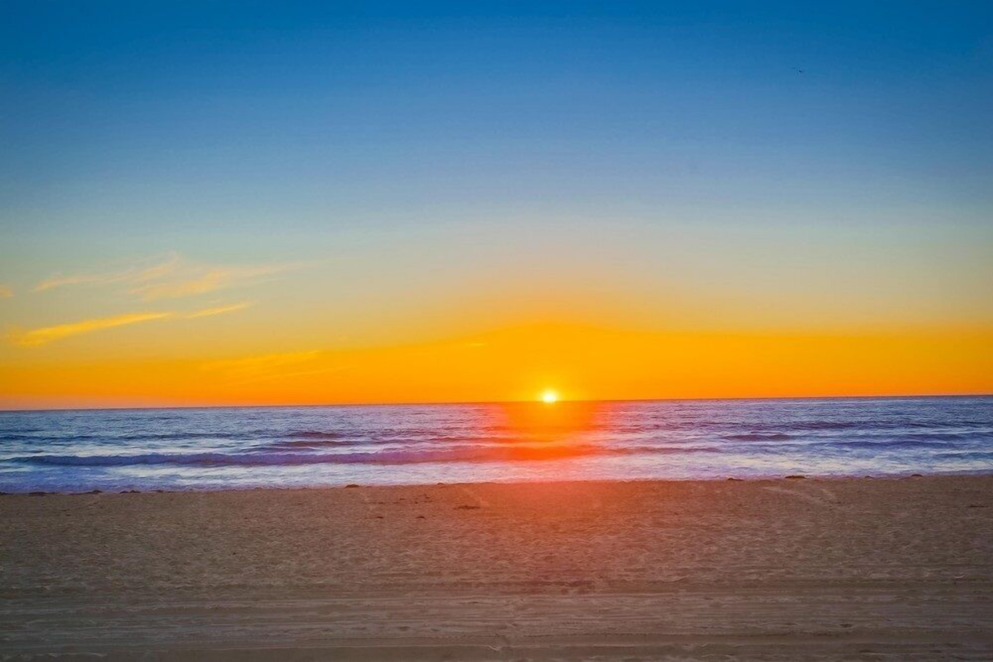 A beach with a sunset over the ocean.