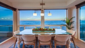 Un coin repas avec une table en verre et des chaises en osier, donnant sur l’océan.