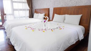 A hotel room with two beds, wooden headboards, white bedding, and a decorative swan made of fabric on the bed.