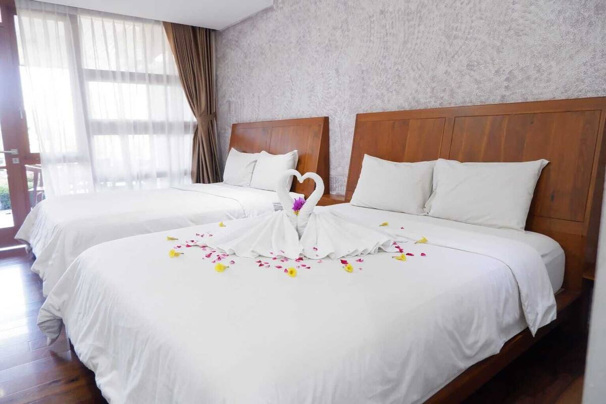 Een hotelkamer met twee bedden, houten hoofdeinden, wit beddengoed en een decoratieve zwaan van stof op het bed.
