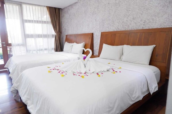 Habitación de hotel con dos camas, cabeceros de madera, ropa de cama blanca y un cisne decorativo hecho de tela sobre la cama.