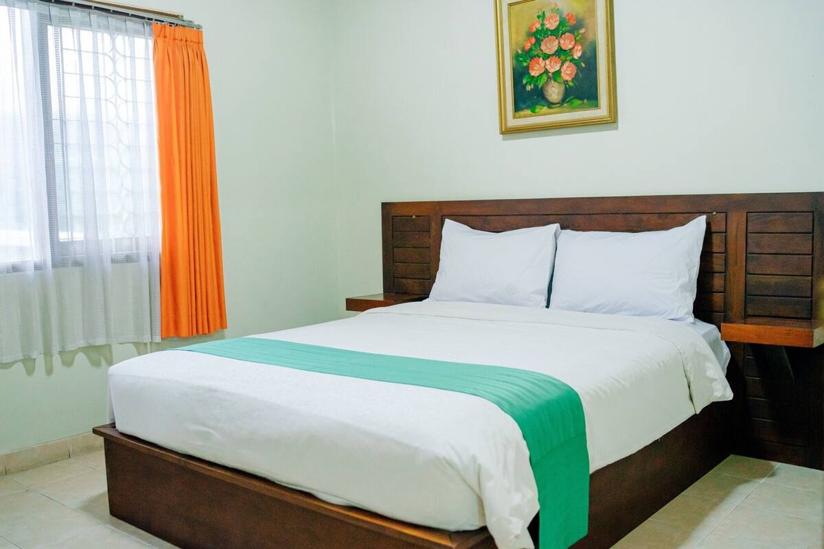 Een netjes opgemaakt bed met een houten hoofdbord, witte beddengoed en een groene accentkleur.