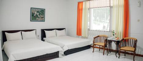 A hotel room with two single beds, a small table with chairs, a window with orange curtains, and a painting on the wall.