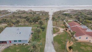 Eine Luftaufnahme eines Wohngebiets mit zwei Häusern, einer asphaltierten Straße und einem Strand im Hintergrund.