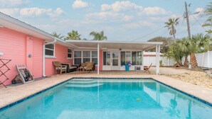 Ein rosafarbenes Haus mit Pool, überdachter Terrasse und umzäunter Garten.