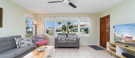 A living room with a grey sofa, a wooden coffee table, a television on a stand, and a ceiling fan.