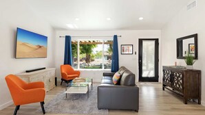 A spacious living room with a sofa, two armchairs, a coffee table, and a view of a garden through a sliding door. - Experience Modern Luxury at Desert Hideaway (Palm Springs)