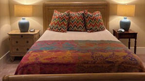 Un dormitorio con una cama grande, dos mesitas de noche con lámparas, una colcha estampada y un cabecero de madera.