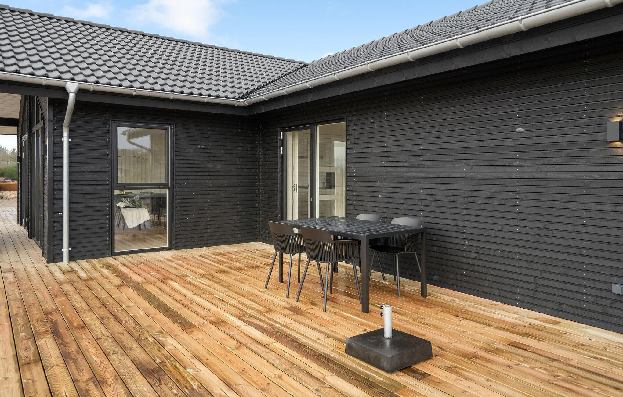Un edificio moderno con una terrazza in legno, un tavolo con sedie e un muro esterno nero.