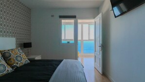A bedroom with a bed, a TV mounted on the wall, and a door leading to a balcony.