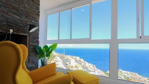 A room with a large window overlooking a coastal city, a yellow armchair, and a black floor lamp.