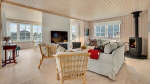 Uma sala de estar aconchegante com sofá, cadeiras, televisão, lareira e janelas grandes.