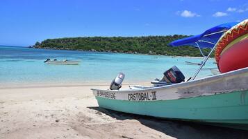 Un bateau nommé « Cristobal II », équipé d’un moteur hors-bord Yamaha, est amarré sur une plage de sable fin, avec une eau turquoise et limpide, et une île boisée en arrière-plan.