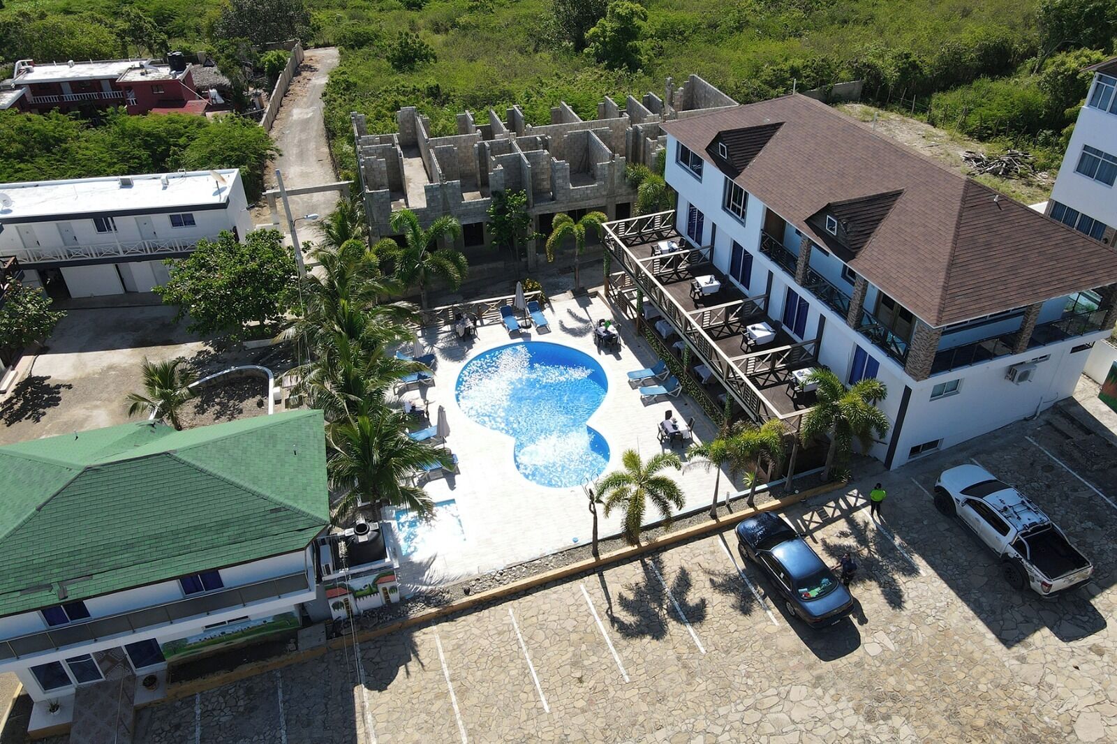 An aerial view of a resort with a swimming pool, multiple buildings, and a parking area.