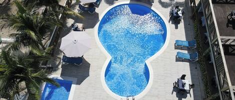 An infinity pool with surrounding lounge chairs and umbrellas, surrounded by palm trees.