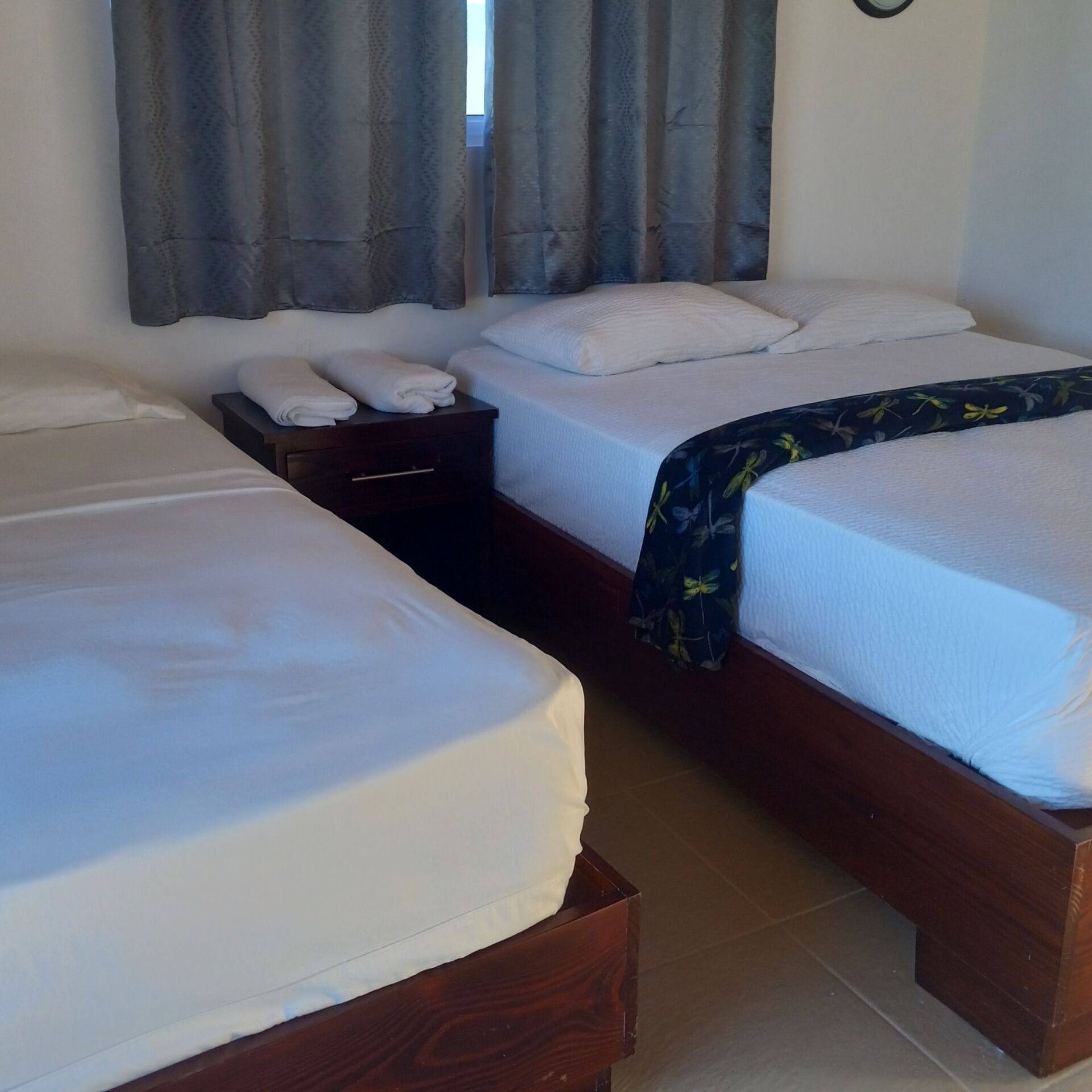 A hotel room with two single beds, a nightstand, and a window with curtains.