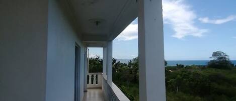A long, narrow balcony with a view of the ocean and greenery.