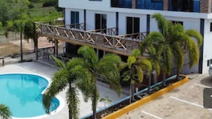 Un bâtiment à deux étages doté d’une piscine, de palmiers et d’un pont en bois.