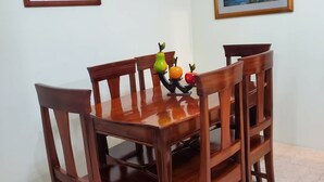 Un comedor con una mesa y sillas de madera, un centro de mesa con fruta y dos cuadros de paisajes en las paredes.