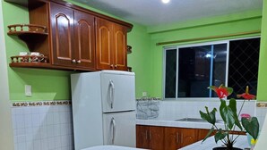Una cocina con armarios de madera, un refrigerador blanco, una encimera blanca, dos taburetes de madera y una planta en maceta.
