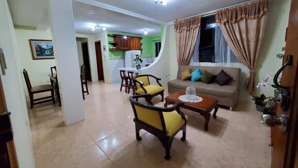 Una sala de estar con un sofá, dos sillones amarillos, una mesa de centro y un comedor con mesa y sillas.