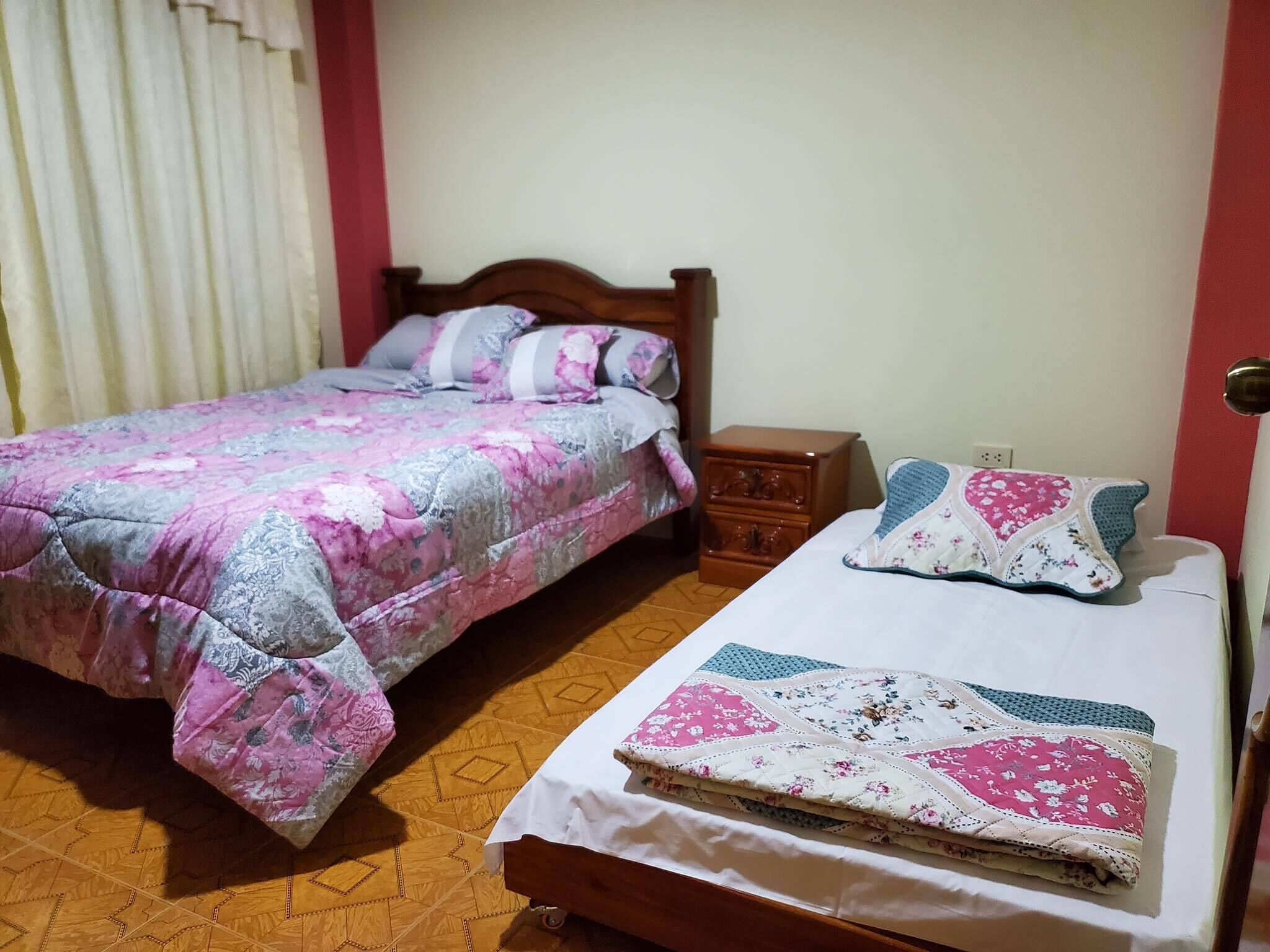 A bedroom with a bed, a nightstand, and a window with curtains.