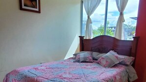 Un dormitorio con cama, ventana con cortinas, un cuadro en la pared y vistas al exterior.
