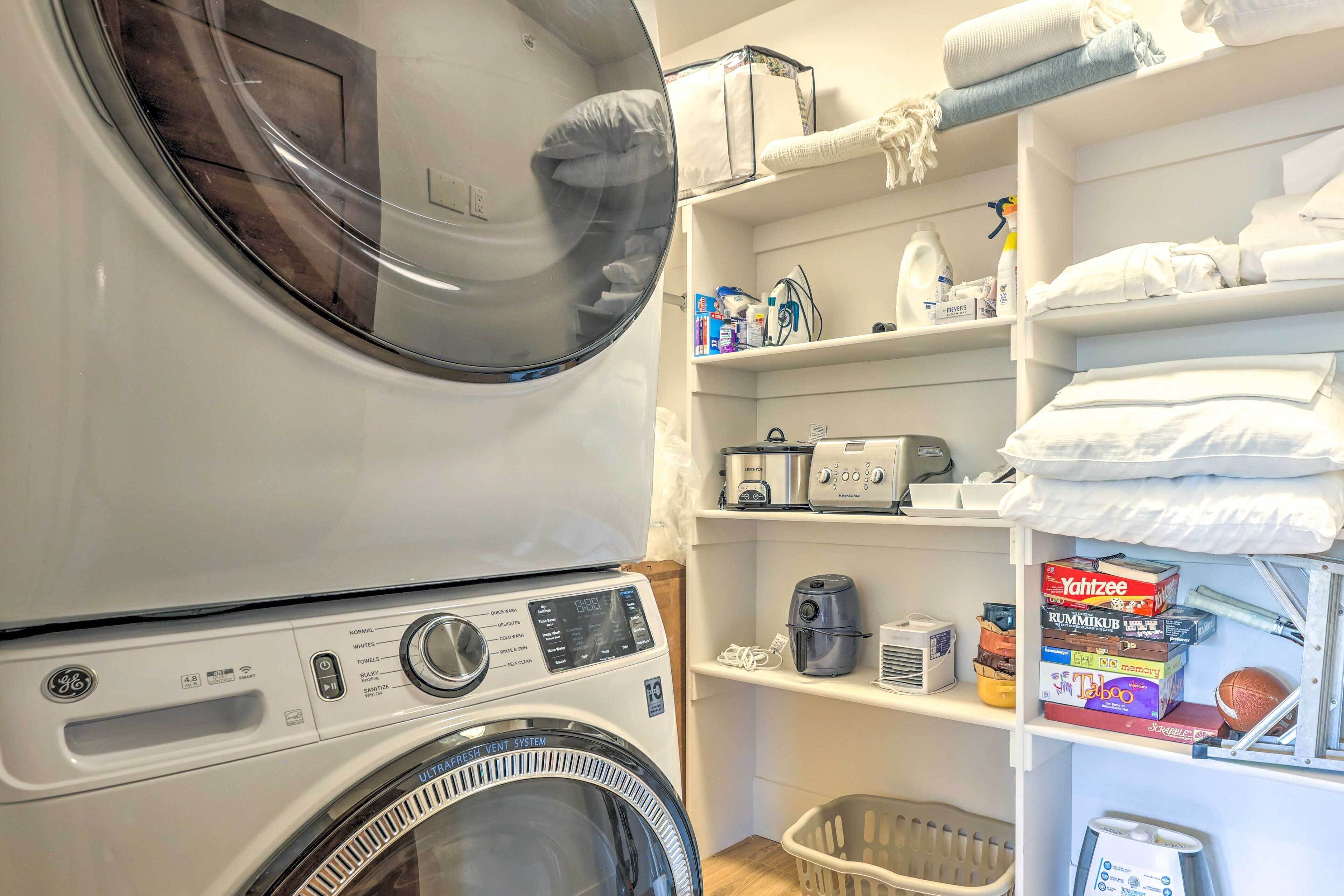 Un espace dédié à la buanderie, comprenant un lave-linge à chargement frontal, des étagères avec des serviettes pliées et divers produits de lessive.