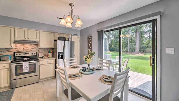 Una cocina moderna con armarios blancos, horno empotrado y comedor con mesa dispuesta para cuatro.