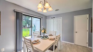 Un comedor con una mesa preparada para cuatro personas, una araña y vistas de un jardín a través de un ventanal corredera.