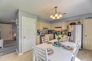 Una cocina moderna con armarios blancos, un refrigerador de acero inoxidable y un comedor con mesa y sillas blancas.