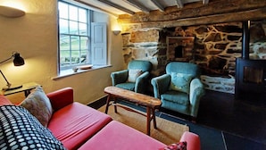 A cozy room with a stone wall, a window, a red sofa, a blue armchair, and a wooden table. - CaeEinion Cottage a Georgeous Rural Retreat Nr Dolgellau (Islawr-dref)