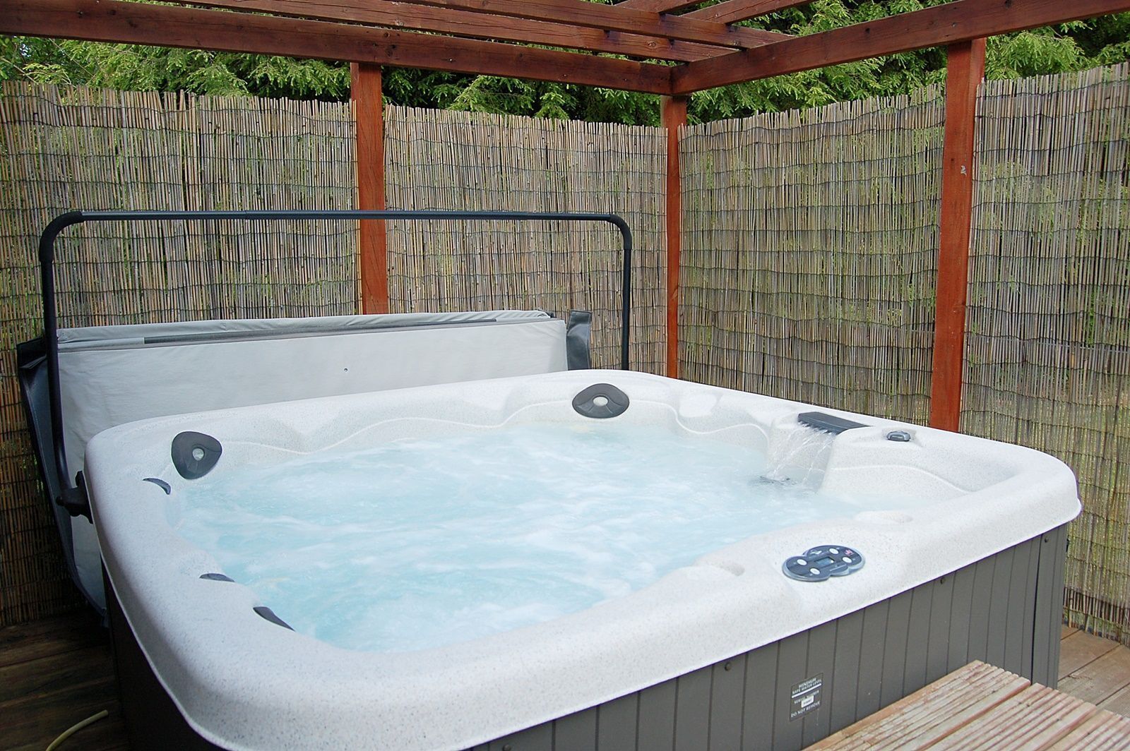 Un bain à remous installé à l’extérieur, surmonté d’une pergola en bois et avec une clôture en bambou en arrière-plan.