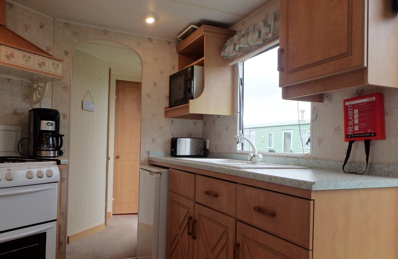 A compact kitchen with a stove, microwave, and coffee maker. There is a window with a view of a house outside.