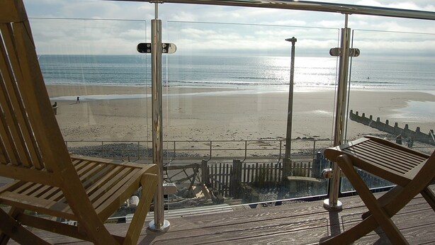 Ein Balkon mit zwei Holzstühlen Blick auf einen Strand.