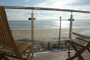 A balcony with two wooden chairs facing a beach. - Chwerthin Y Mor Beach House (Gwynedd)