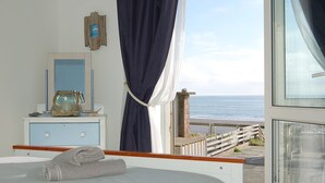 Ein Schlafzimmer mit Bett, Schminktisch, Spiegel und Meerblick durch ein Fenster.
