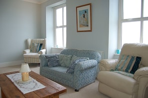 Ein Wohnzimmer mit einem gemusterten Sofa, einem gestreiften Sessel, einem Holztisch und einem Bild an der Wand.