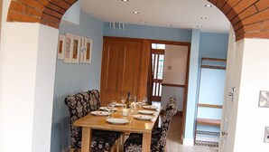 A dining area with a brick archway, a wooden table set for four, and patterned chairs. - Idris View Family Holiday Home (Tywyn)
