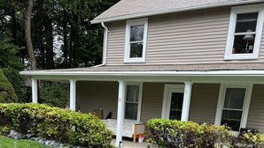 A two-story house with a covered porch, a front yard with grass and bushes, and a small garden with pink flowers. - Entire 3 bedrooms/2 bathrooms fence yard, near Costco, Sam's (Gaithersburg)